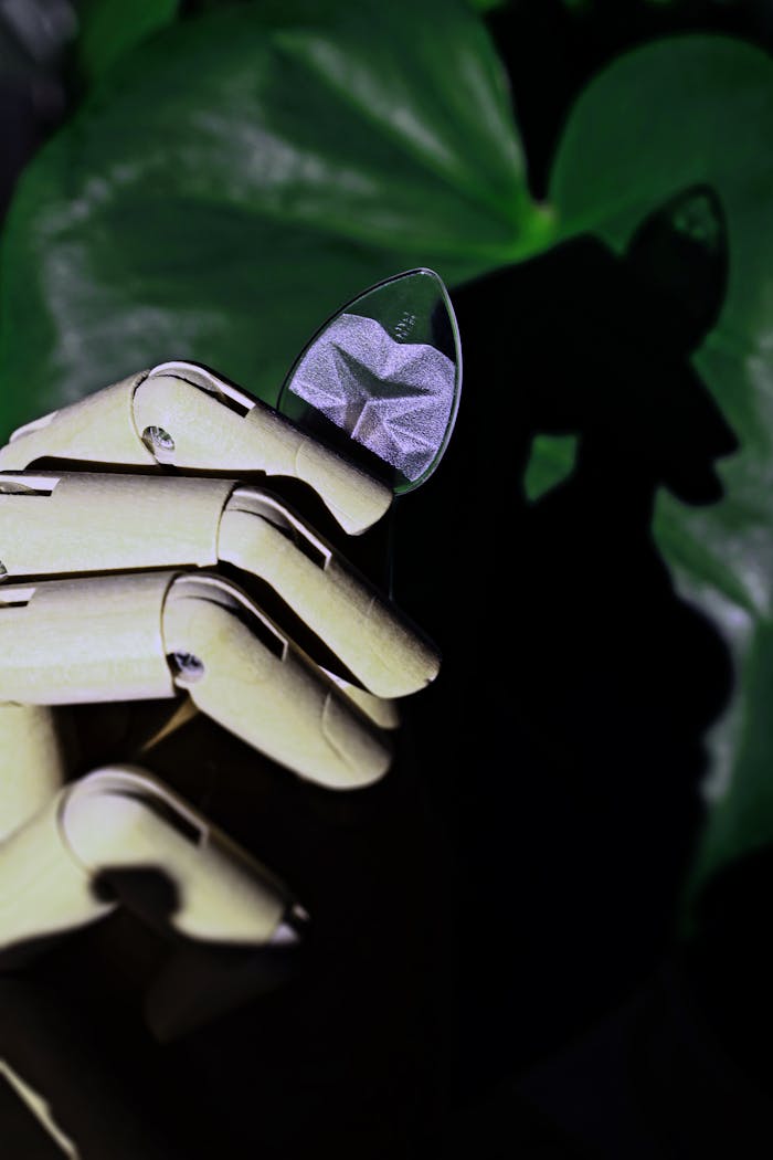 Close-up of a wooden robotic hand holding a guitar pick against a green background.